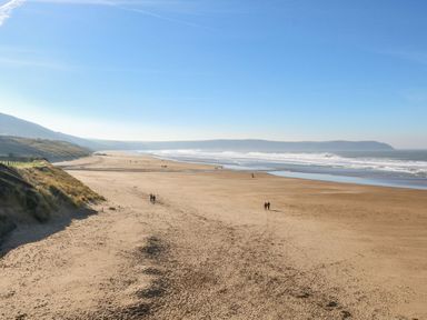 A wide sandy beach with small groups of people walking near the shoreline and hills in the background at Burr 2 Shepherds Hut in Swimbridge near Barnstaple