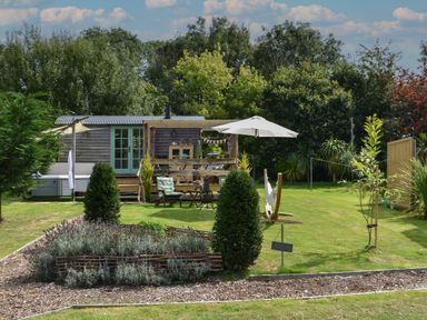 A garden with a small wooden hut a seating area with umbrella and hammock in the lawn at Burr 2 Shepherds Hut in Swimbridge near Barnstaple