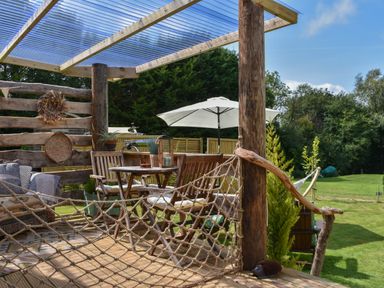 An outdoor seating area with wooden chairs and table under a clear roof and a white umbrella on a grassy lawn at Burr 2 Shepherds Hut Swimbridge near Barnstaple