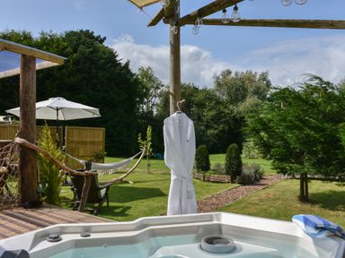An outdoor area with a hot tub a wooden deck chairs hammock and umbrella at Burr 2 Shepherds Hut in Swimbridge near Barnstaple