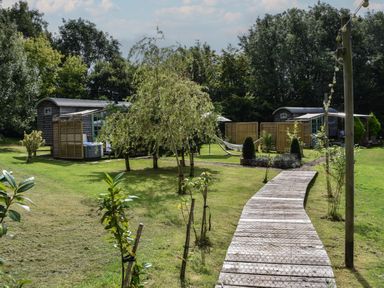 A garden area with two wooden huts a wooden pathway trees and a hammock at Burr 2 Shepherds Hut Swimbridge near Barnstaple