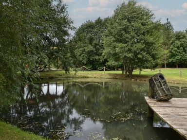 A pond with trees around it and a wooden dock with a crab pot at Burr 2 Shepherds Hut in Swimbridge near Barnstaple