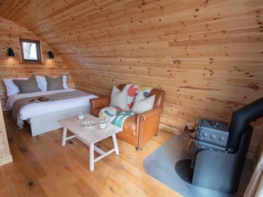 A wooden room with a bed a leather sofa a small wooden table and a wood-burning stove at Glamping Pod 1 Comfort in Lebberston