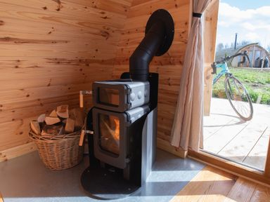 A wood stove with a basket of firewood inside a wooden room next to a door with a bicycle outside at Glamping Pod 1 Comfort in Lebberston