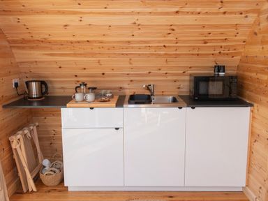 A small kitchen with a kettle cups a sink and a microwave in a wooden room at Glamping Pod 1 Comfort in Lebberston