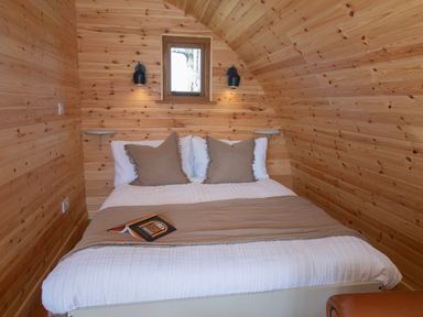 A bedroom with a bed with white bedding and beige pillows under a small window in a wooden room at Glamping Pod 1 Comfort in Lebberston