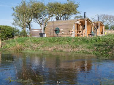 Two wooden glamping pods near a pond with picnic tables and a hot tub at Glamping Pod 1 Comfort in Lebberston