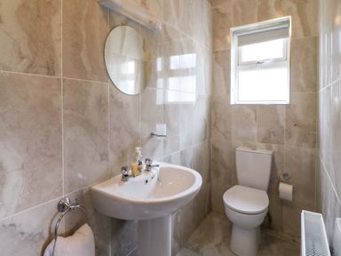 A bathroom with a sink a round mirror a toilet and a window at No 1 Lodge Wood in Kenmare County Kerry