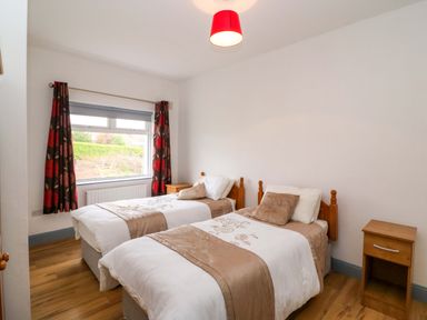 A bedroom with two single beds two bedside tables and a window with curtains at No 1 Lodge Wood in Kenmare County Kerry