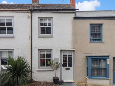 The front exterior of a small two-story house with white walls and a door with windows at Cobblestone Cottage in Bude