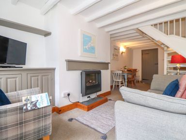 A living room with a TV on a cabinet a fireplace sofas and a dining table at Cobblestone Cottage in Bude