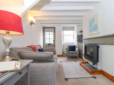 A sitting room with a gray sofa a red lamp a plaid armchair a rug a fireplace and a television at Cobblestone Cottage in Bude