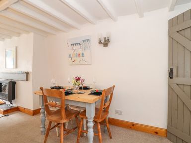 A dining area with a wooden table and four chairs with place settings and a floral centerpiece at Cobblestone Cottage in Bude
