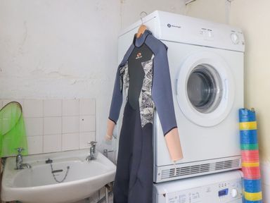 A laundry room with a washing machine and dryer stacked a wetsuit hanging on the dryer a sink and a colorful rolled mat near Cobblestone Cottage in Bude