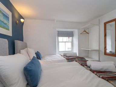 A bedroom with two single beds blue pillows towels on beds a window and wall shelves at Cobblestone Cottage in Bude