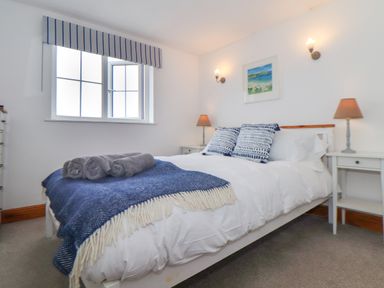 A bedroom with a double bed two bedside tables with lamps a window and a framed picture on the wall at Cobblestone Cottage in Bude