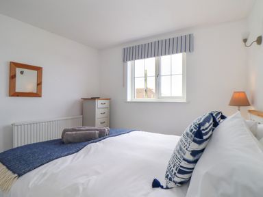 A bedroom with a bed pillow towel chest of drawers window and wall mirror at Cobblestone Cottage in Bude