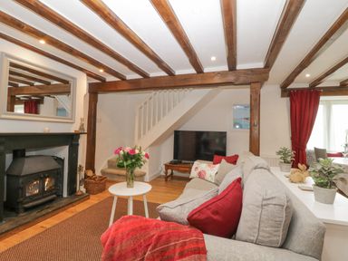 A living room with a wood burning stove a sofa a coffee table with flowers and wooden beams on the ceiling at 4 Barton Cottages in Down Thomas near Plymouth