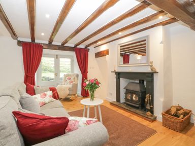 A living room with a grey sofa red curtains a rocking chair and a fireplace at 4 Barton Cottages Down Thomas near Plymouth