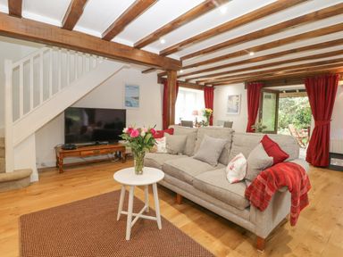 A living room with a gray sofa and red curtains near a dining table and TV at 4 Barton Cottages in Down Thomas near Plymouth