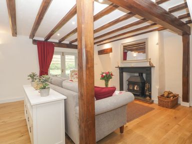 A living room with wooden beams a fireplace a sofa and red curtains at 4 Barton Cottages Down Thomas near Plymouth