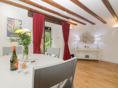 A dining room with a table set with flowers wine and glasses and red curtains at 4 Barton Cottages in Down Thomas near Plymouth