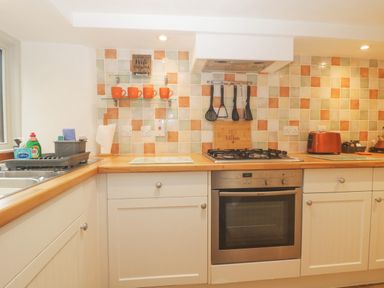 A kitchen with a gas stove oven orange mugs on shelves and a toaster at 4 Barton Cottages Down Thomas near Plymouth