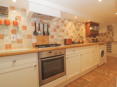 A kitchen with tiled backsplash stove oven washing machine and wooden countertops at 4 Barton Cottages Down Thomas near Plymouth