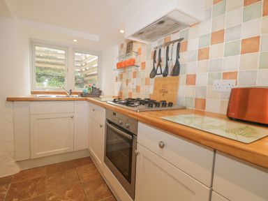 A kitchen with a sink by a window an oven and stovetop with cooking utensils and a toaster on the counter at 4 Barton Cottages in Down Thomas near Plymouth