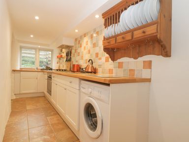 A narrow kitchen with white cabinets wooden countertop washing machine and plate rack at 4 Barton Cottages Down Thomas near Plymouth