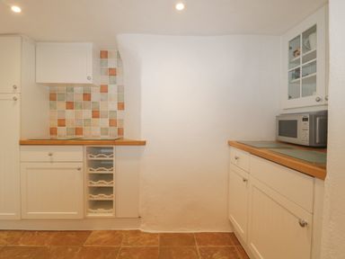 A kitchen with white cabinets a tiled backsplash a microwave on the countertop and wooden edges at 4 Barton Cottages Down Thomas near Plymouth