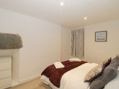 A bedroom with a bed with pillows and towels and a chest of drawers with a stone lintel above at 4 Barton Cottages in Down Thomas near Plymouth
