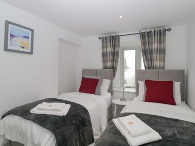 A bedroom with two single beds a window with plaid curtains and a small round table with a lamp between beds at 4 Barton Cottages Down Thomas near Plymouth