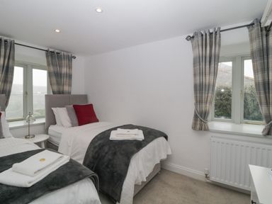 A bedroom with two single beds with gray and red pillows and plaid curtains at 4 Barton Cottages in Down Thomas near Plymouth