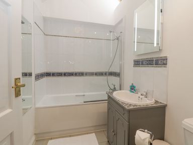 A bathroom with a bathtub and shower, sink with vanity cabinet, mirror, and toilet paper holder at 4 Barton Cottages Down Thomas near Plymouth