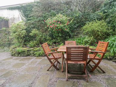 An outdoor patio with wooden table and four chairs surrounded by plants at 4 Barton Cottages Down Thomas near Plymouth
