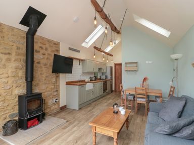 A kitchen area with wooden countertops and a dining table with chairs next to a living space with a couch and a wood burning stove at The Cart Shed in Barwick near Yeovil Somerset