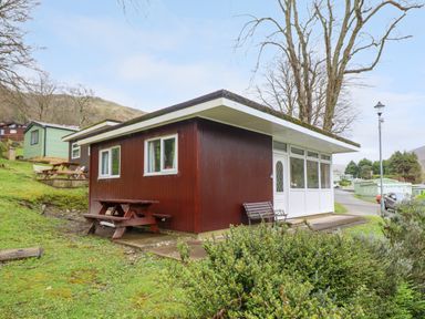 A small wooden cabin with white windows and a door a picnic bench and benches outside on grass at Hill View in Bryncrug near Tywyn