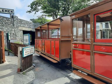 A red and brown vintage train next to a stone tunnel entrance with a passengers must not pass here sign