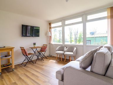 A living room with wooden floor a wall mounted TV two armchairs a small table with two chairs and a sofa at Hill View in Bryncrug near Tywyn