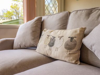 A beige sofa with a decorative pillow featuring sheep designs by a window at Hill View in Bryncrug near Tywyn