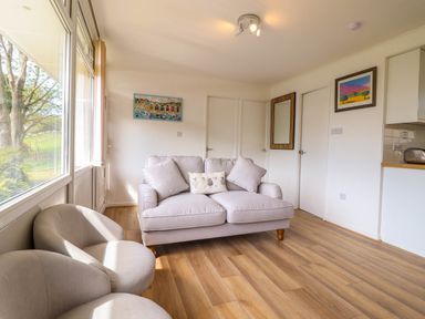 A living room with a sofa, two armchairs, wall paintings, a mirror, and large windows at Hill View in Bryncrug near Tywyn
