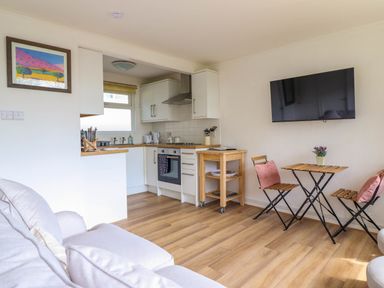 A kitchen with white cabinets a wooden table with two chairs and a wall mounted TV at Hill View in Bryncrug near Tywyn