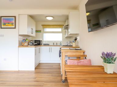 A kitchen with white cabinets microwave and wooden table with chair and purple flowers at Hill View Bryncrug near Tywyn