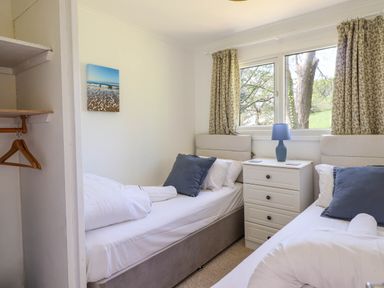 A bedroom with two single beds a nightstand with a lamp and a window with curtains at Hill View in Bryncrug near Tywyn