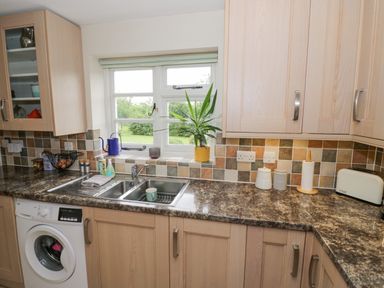 A kitchen with wooden cabinets a double sink a washing machine and a window overlooking a garden at Orchard View in Redmary D Abitot near Hartpury