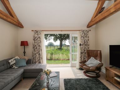 A living room with a gray sectional sofa a brown leather chair a coffee table and large window showing a tree at Orchard View in Redmary D'Abitot near Hartpury