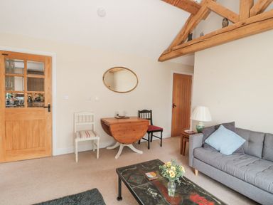A living room with a gray sofa, wooden coffee table with flowers, small wooden table with lamp, two chairs, and a wooden drop-leaf table at Orchard View Redmary D Abitot near Hartpury