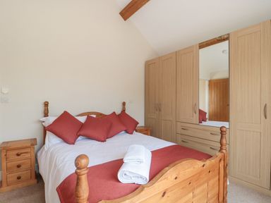 A bedroom with a wooden bed with white bedding and red pillows and blanket next to wooden wardrobes and a bedside table at Orchard View in Redmary D Abitot near Hartpury