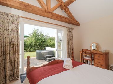 A bedroom with a bed with towels on it a wooden dressing table and chair and a view of a garden with a hot tub at Orchard View in Redmary D'Abitot near Hartpury